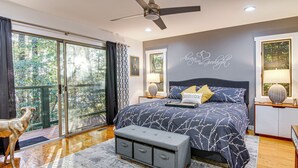 A bedroom with a large bed, a ceiling fan, and a view of trees through the window. - Festive Lakefront Escape: Blue Ridge Holiday Home (Brevard)