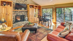 A cozy living room with a stone fireplace, leather furniture, and a large TV. - Festive Lakefront Escape: Blue Ridge Holiday Home (Brevard)
