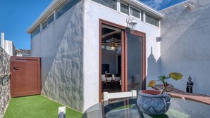 Un bâtiment moderne avec une entrée dotée d’une porte en verre, un petit patio avec une table et des chaises, et une plante en pot.