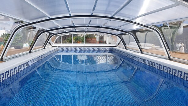 Une piscine dotée d’un sol carrelé d’un bleu éclatant et d’une structure de toit en verre.
