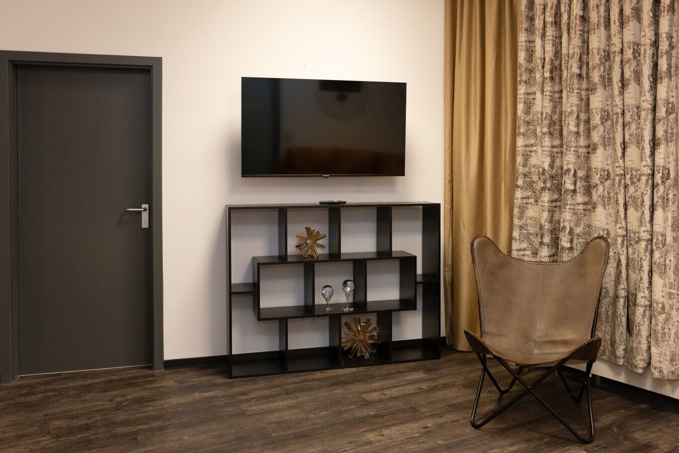 Ein modernes Wohnzimmer mit dunklem Holzboden, einer schwarzen Unterhaltungsanlage mit Dekoration, einem Wand-Fernseher und einem braunen Ledersessel.