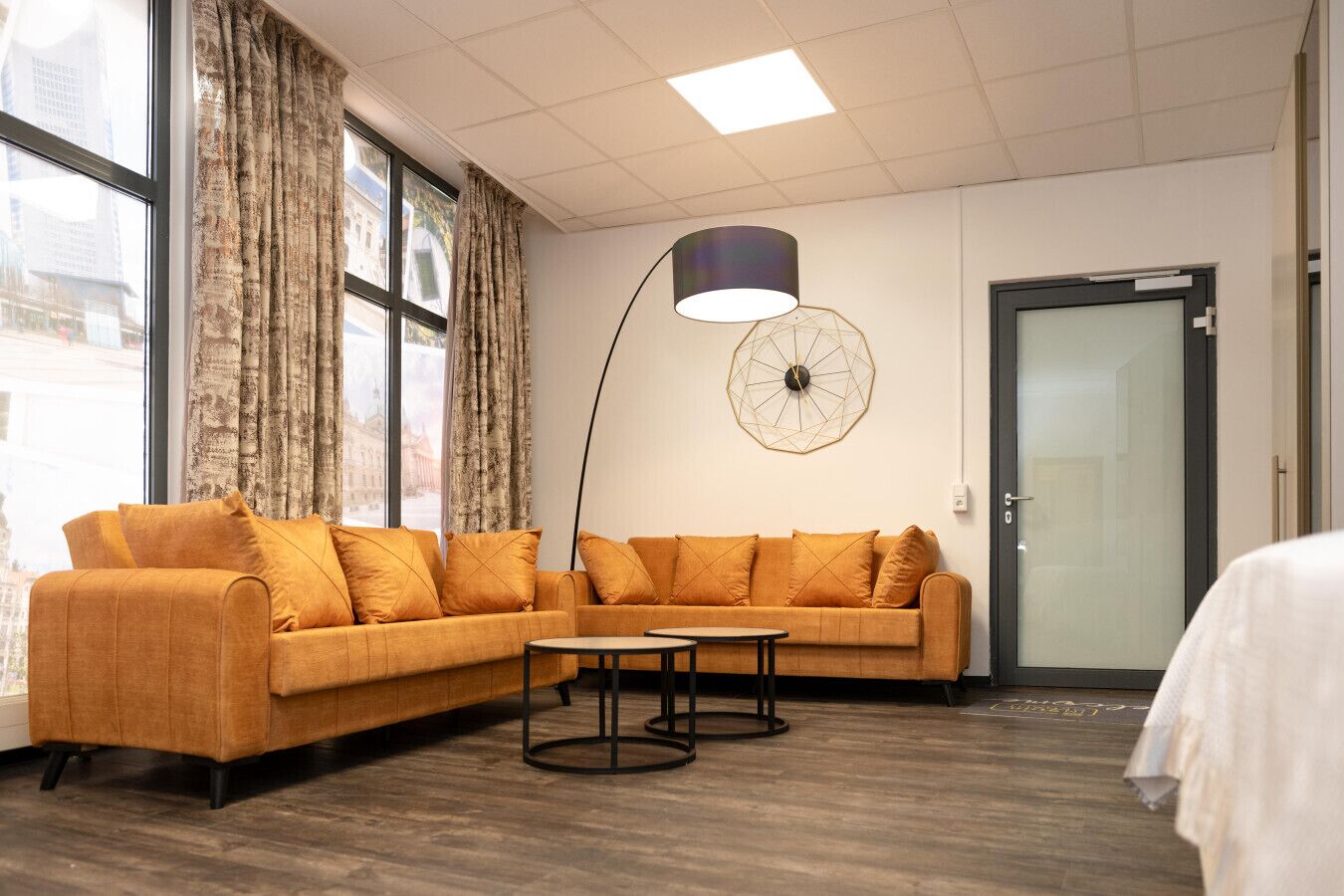 Una habitación moderna con un sofá seccional, una mesa de centro redonda, una lámpara de pie y vistas de la ciudad a través de grandes ventanales.