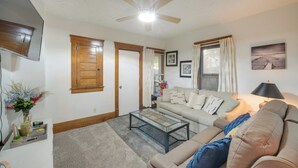 Un salon avec un ventilateur de plafond, un canapé, une table basse et un téléviseur fixé au mur.