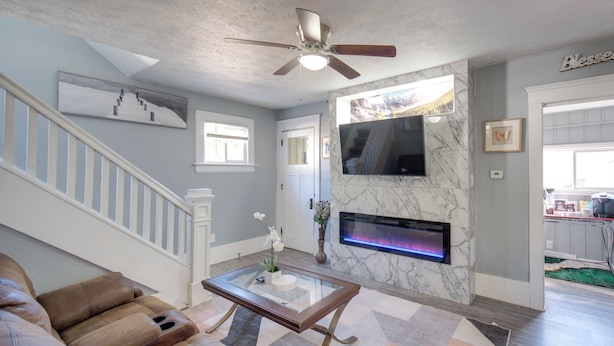 Una sala de estar con un sofá, una mesa de centro de vidrio, una chimenea, un televisor montado en la pared y una escalera.
