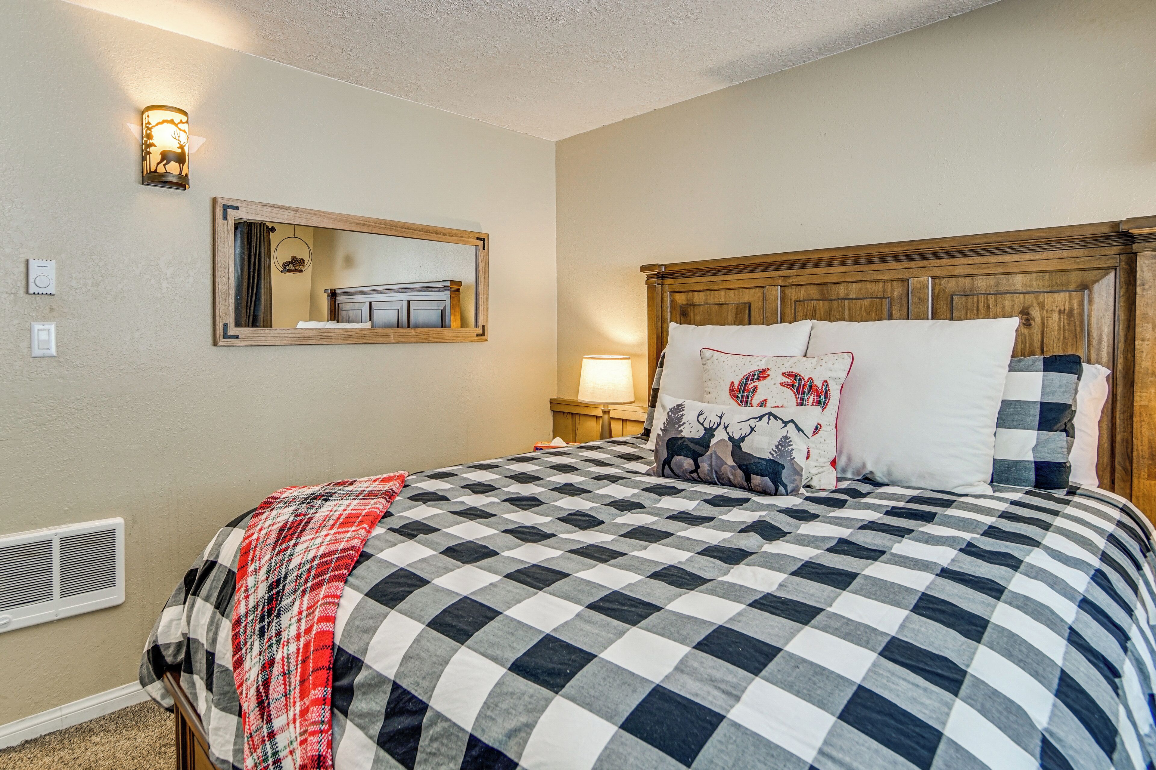 A bedroom with a large bed, a wooden headboard, a mirror, a wall-mounted light, and a bedside table with a lamp.