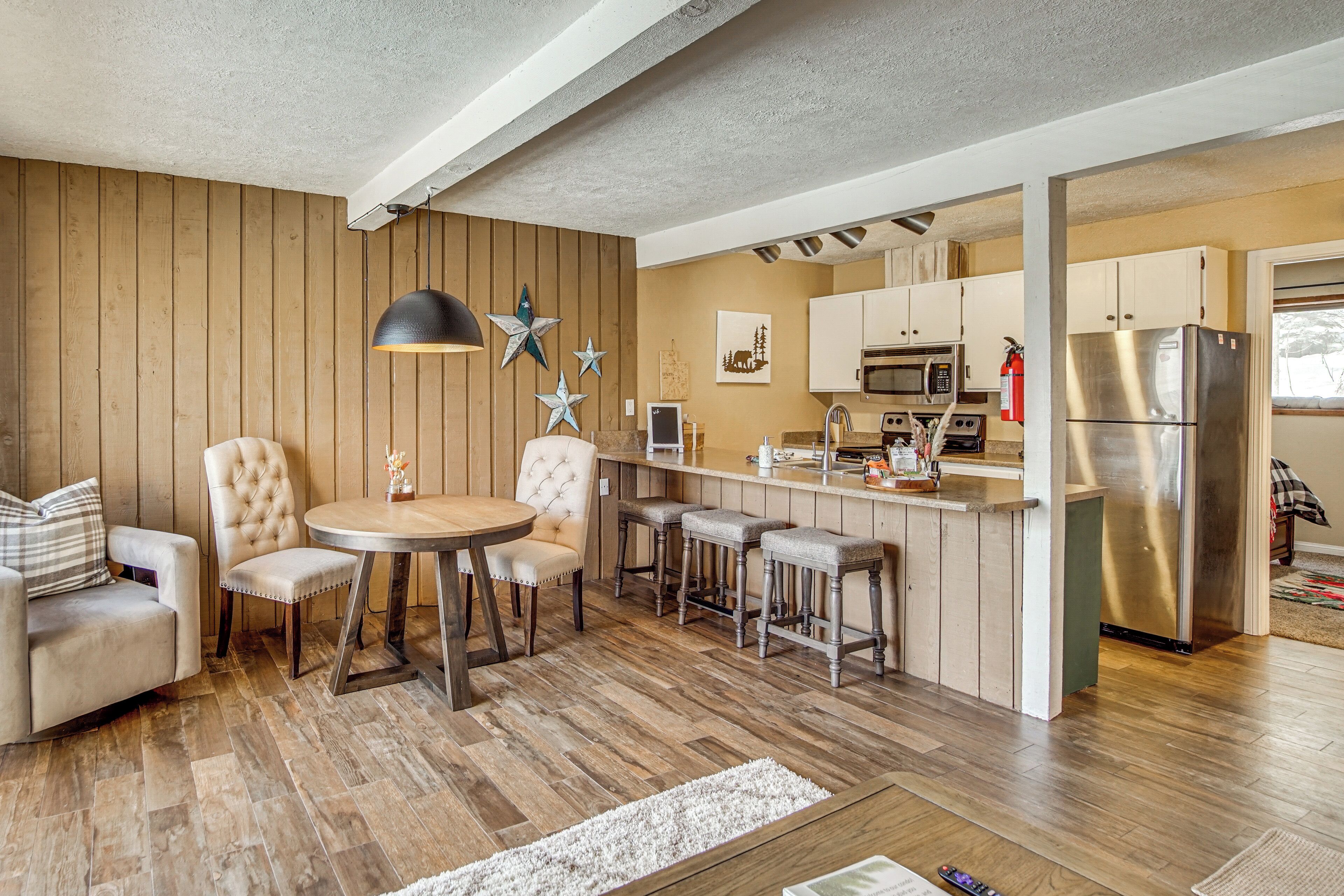 Une cuisine moderne avec un lambris en bois, un îlot central doté de tabourets, un réfrigérateur en acier inoxydable et un coin repas avec une table ronde et des chaises rembourrées.