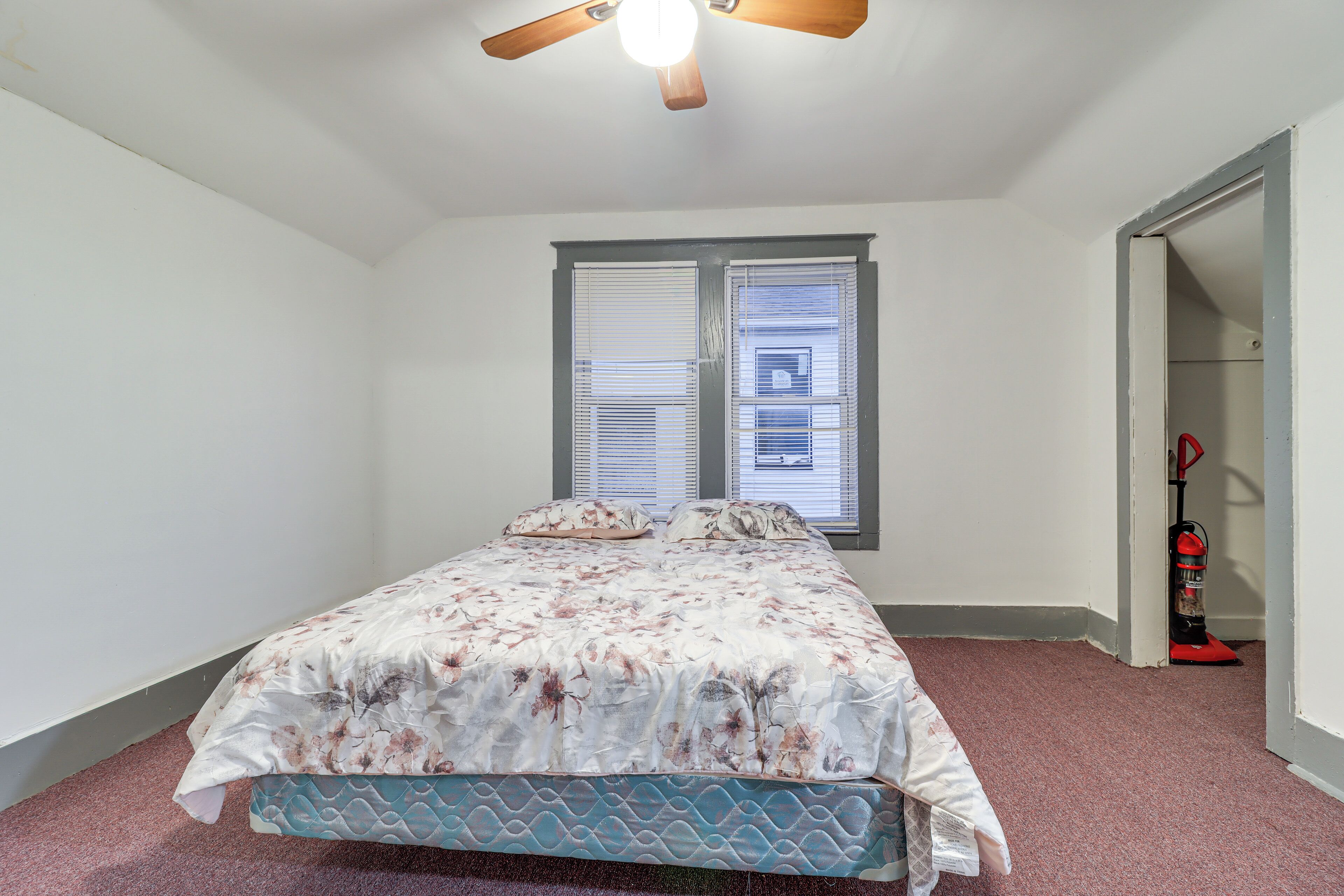 Une chambre à coucher avec un lit, un ventilateur de plafond et une fenêtre avec des stores.