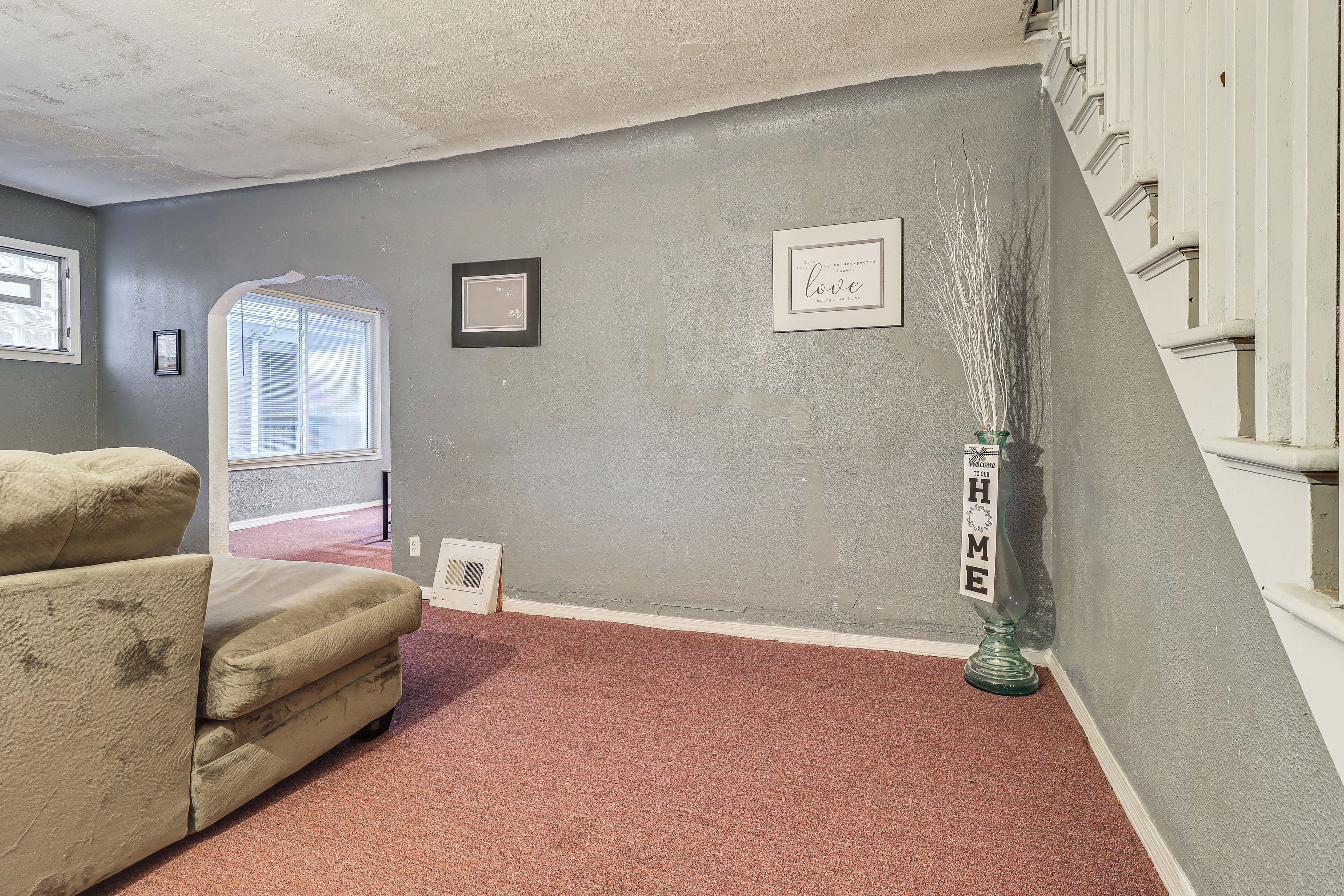 A living room with a grey wall, a beige sofa, a red carpet, and a framed picture with the word "love".