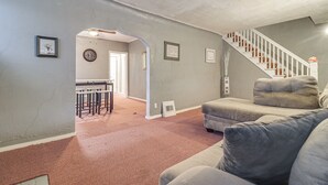 A living room with a grey couch, a staircase, and a kitchen area in the background. - Easy Dtwn Detroit Access: Pet-friendly Family Home (Detroit)
