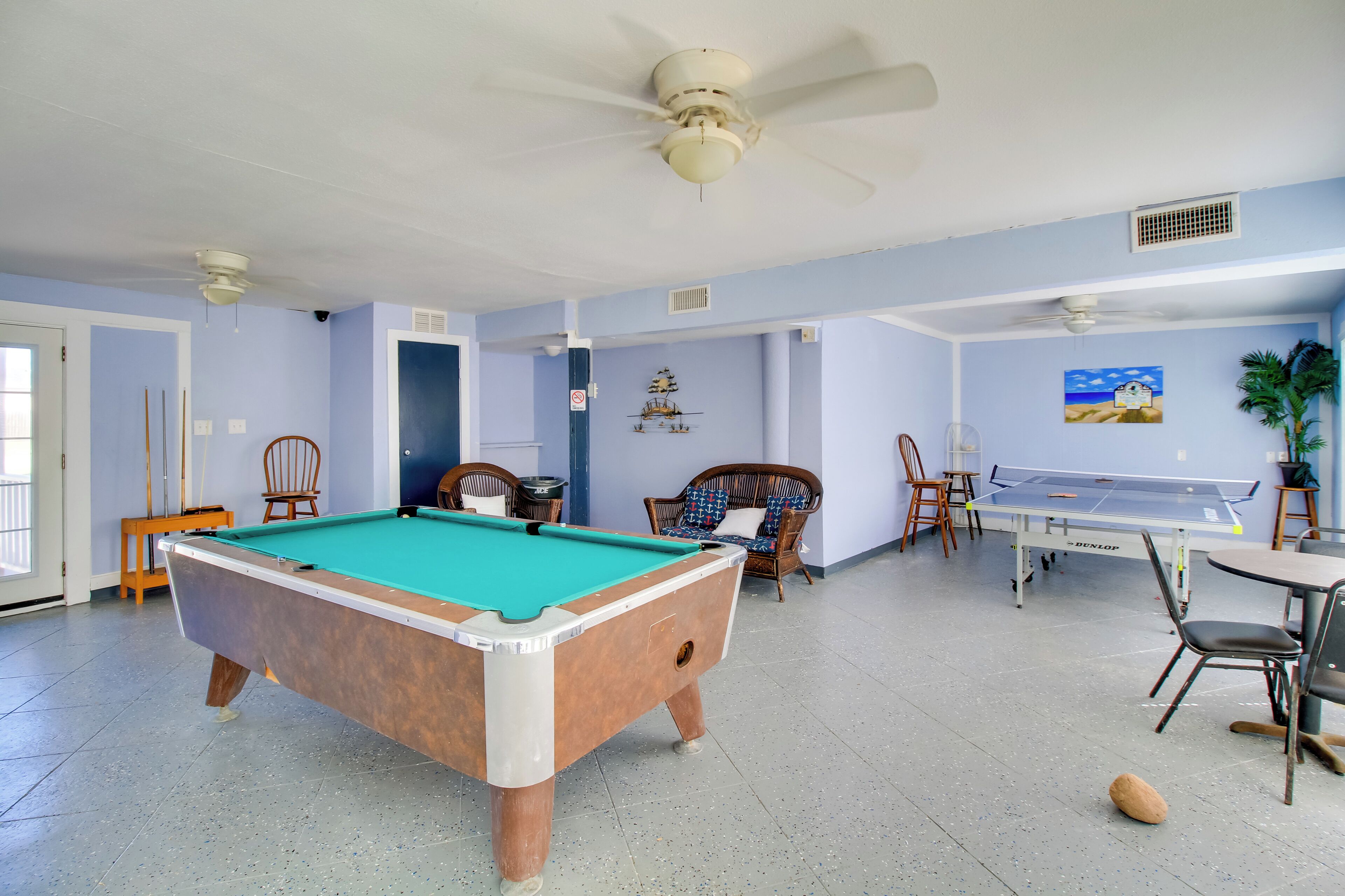 A pool table, chairs, and a ping pong table in a room with light blue walls and ceiling fans.