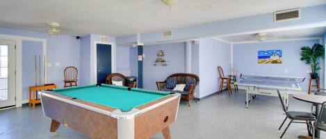 A pool table, chairs, and a ping pong table in a room with light blue walls and ceiling fans.