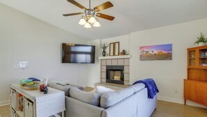 A living room with a grey sofa, a flat-screen TV mounted on the wall, a fireplace, and a ceiling fan. - Family Home, 7 Mi to Joshua Tree National Park! (Twentynine Palms)