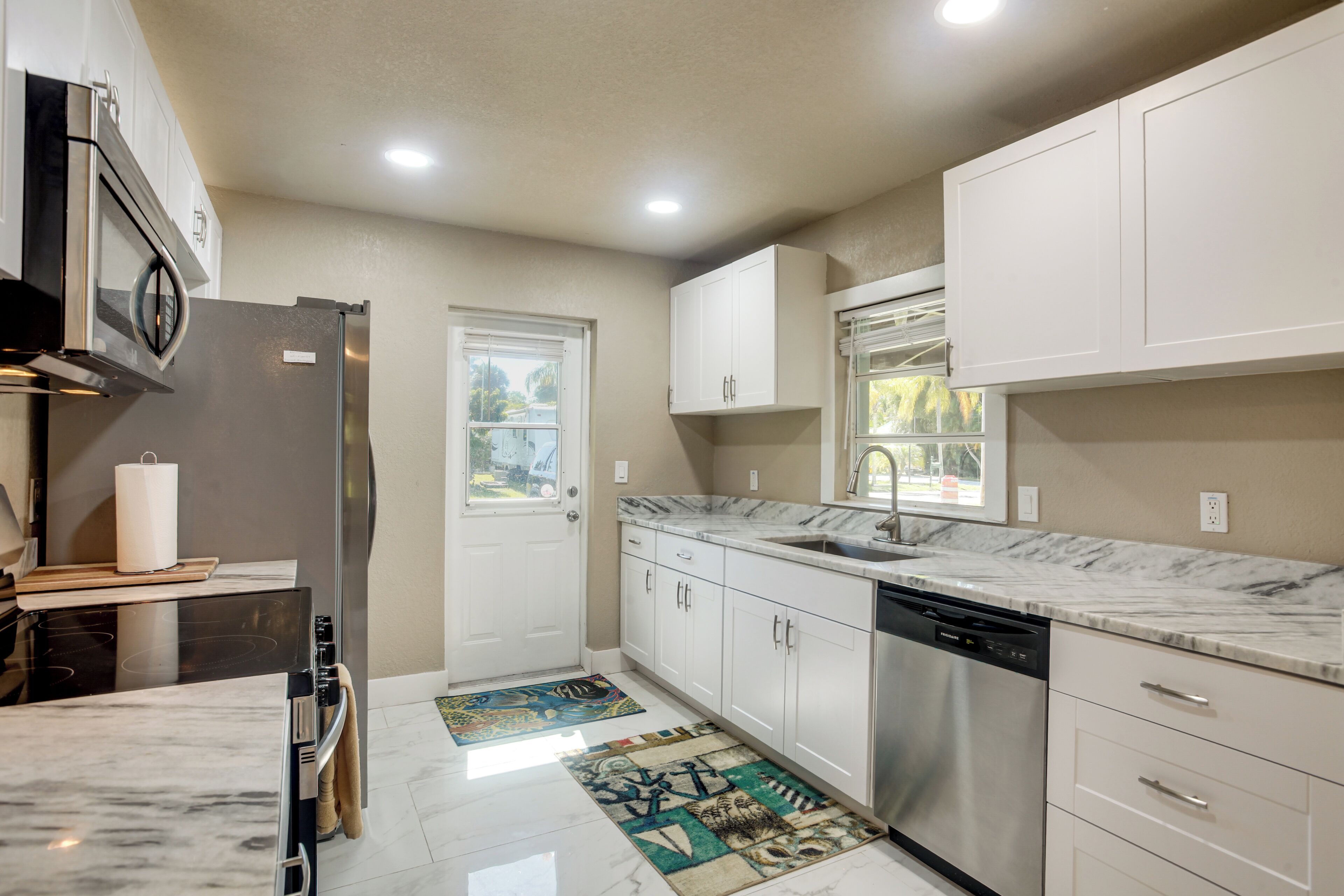 A modern kitchen with white cabinets, stainless steel appliances, and a marble countertop.