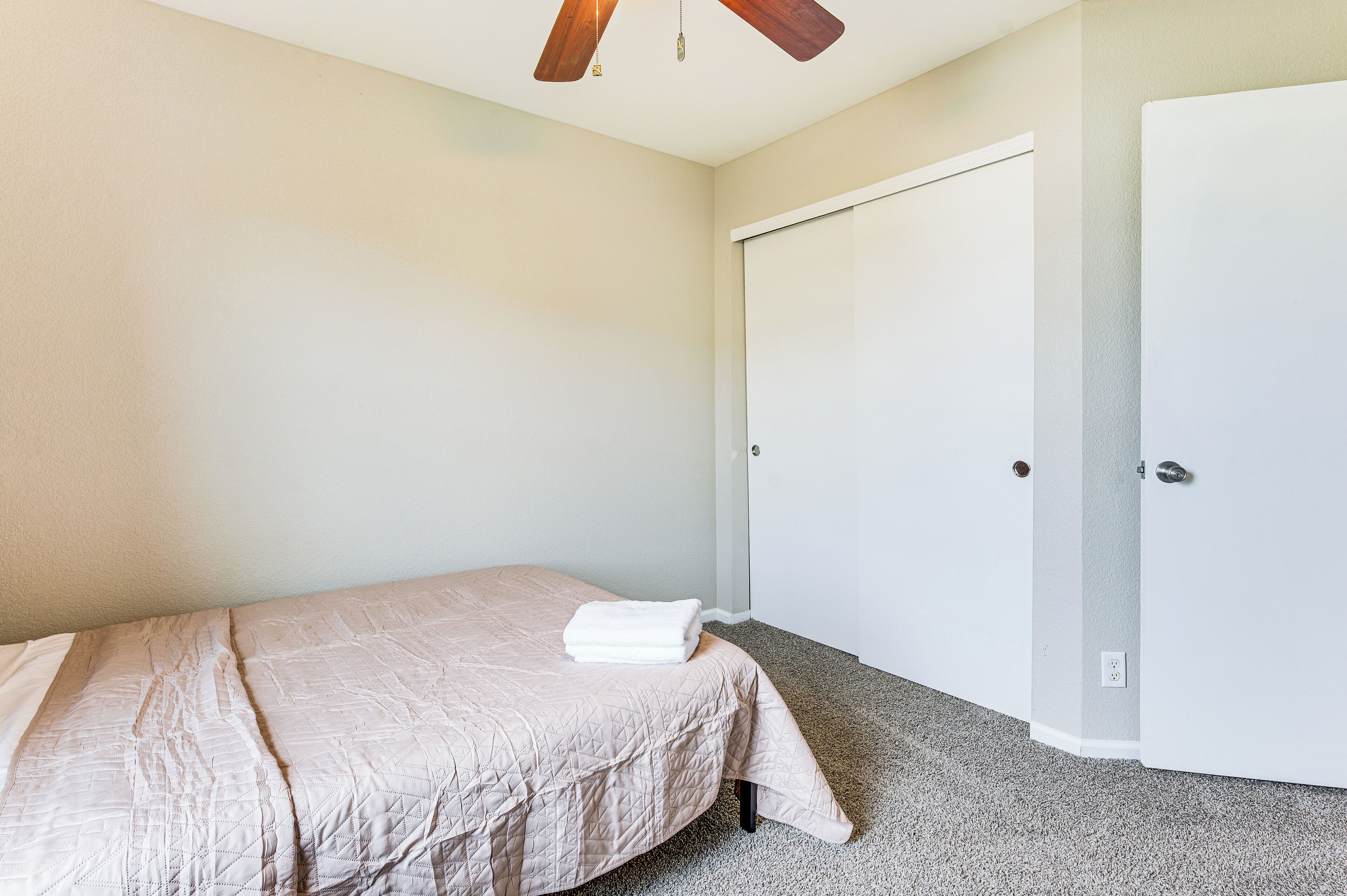 A bedroom with a bed, a ceiling fan, and a white door.