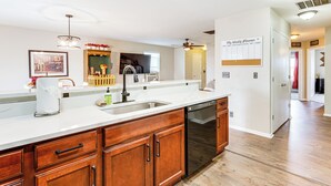 A modern kitchen with wooden cabinets, a stainless steel dishwasher, and a white countertop. - Fenced-in Yard w/ Deck: Pet-friendly Lochbuie Home (Brighton)