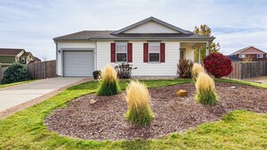 A single-story house with a garage, a front yard with mulch and grass, and a red bush. - Fenced-in Yard w/ Deck: Pet-friendly Lochbuie Home (Brighton)