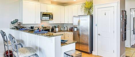 A kitchen with white cabinets, stainless steel appliances, and a center island with bar stools.
