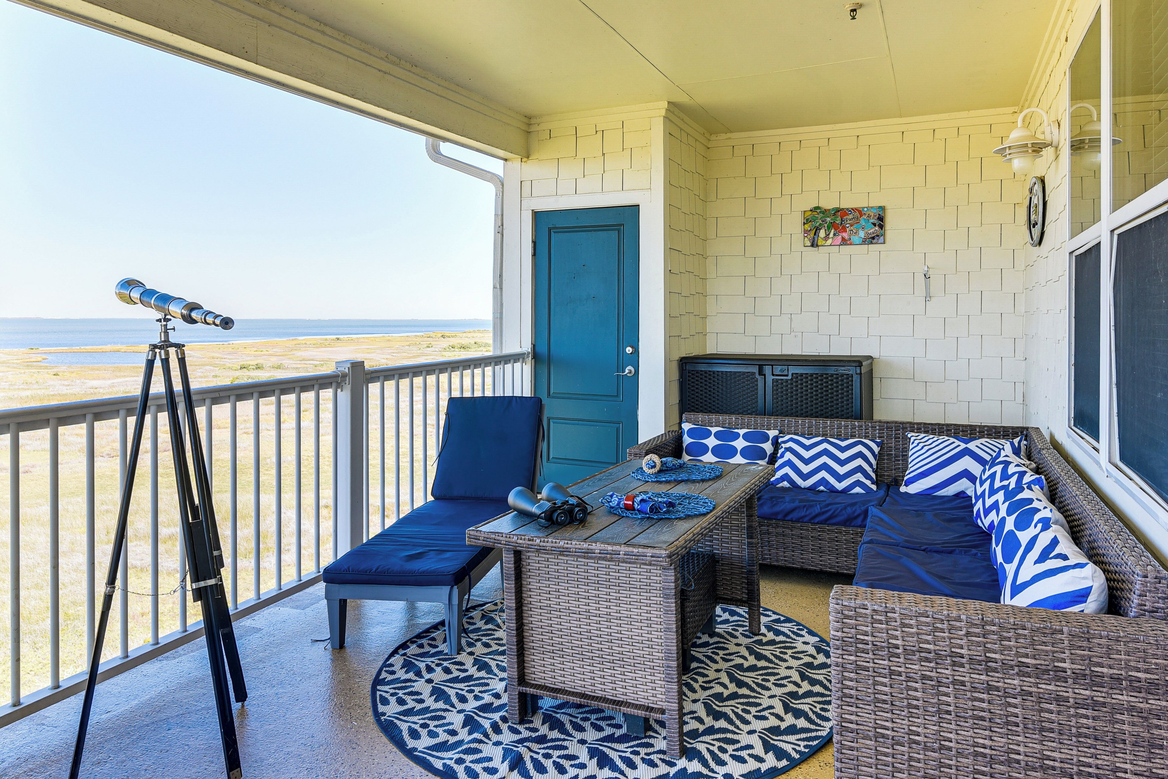 A balcony with a telescope, wicker furniture, and a view of the beach.