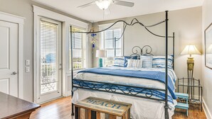 A bedroom with a four-poster bed, a ceiling fan, and a view through the window blinds. - Steps to Private Beach: Galveston Resort Condo! (Galveston)
