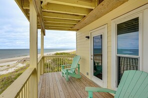 Une terrasse en bois avec deux fauteuils Adirondack verts et une porte vitrée donnant sur un balcon avec vue sur la plage.