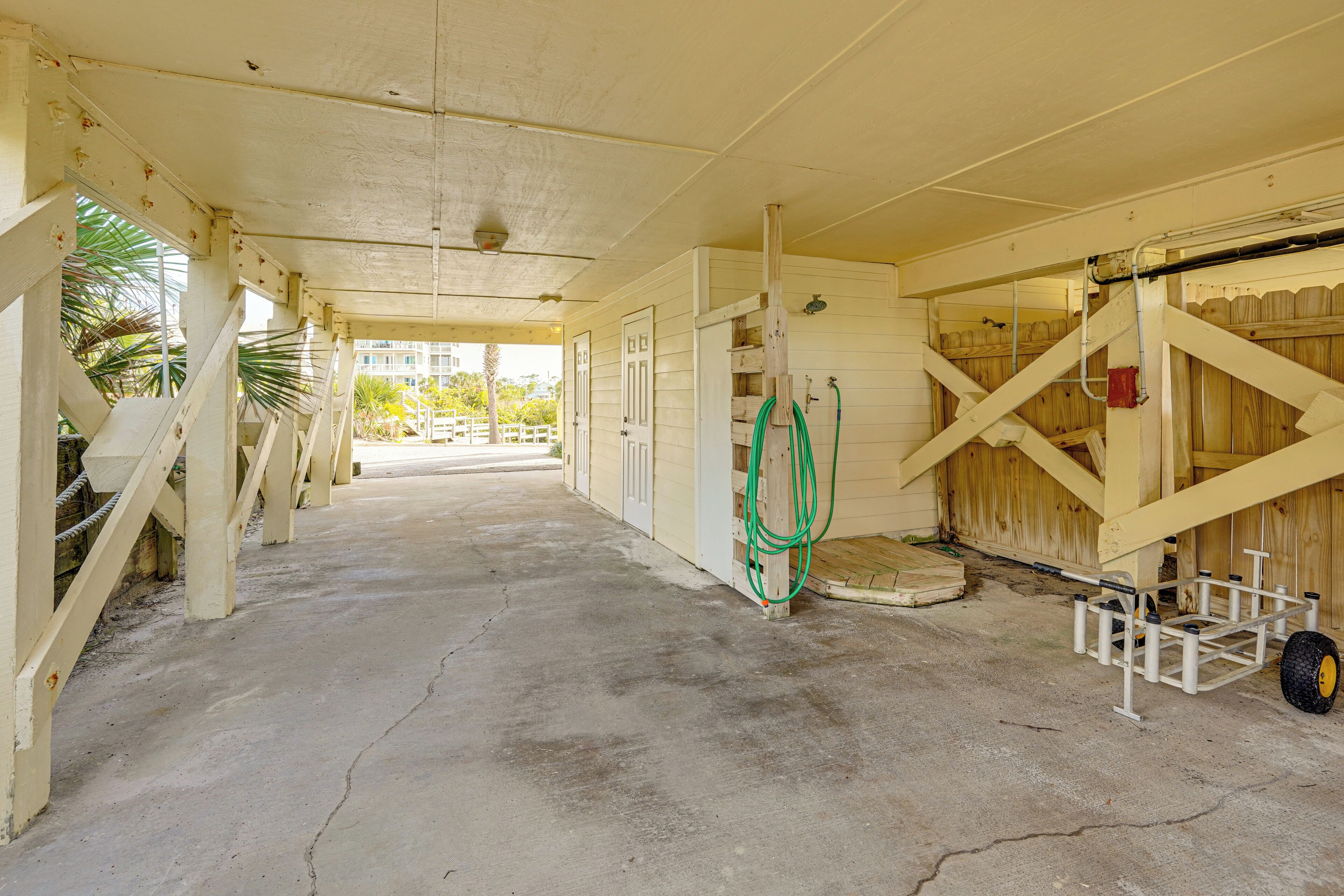 A covered outdoor area with a concrete floor, wooden structures, and a green hose.