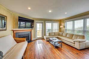 Un salon avec une cheminée, un canapé beige, un canapé d’angle et un plancher en bois.