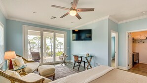 Une chambre à coucher comprenant un lit, une table en verre, une chaise, un ventilateur de plafond et un téléviseur.