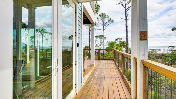 Une terrasse en bois avec des portes vitrées donnant sur un balcon qui offre une vue sur la plage.