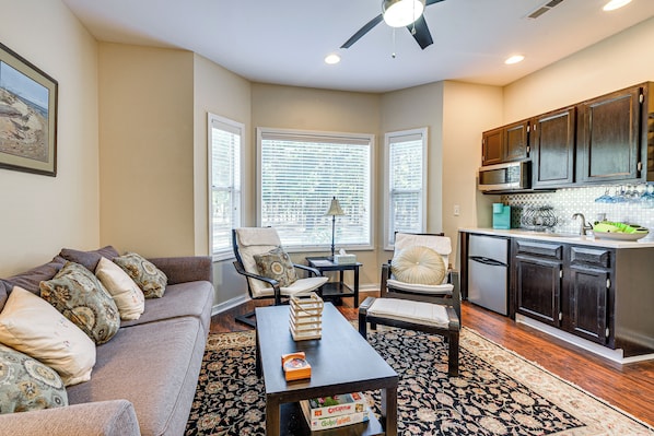 A living room with a sofa, chairs, a coffee table, and a kitchen area with cabinets and appliances. - Fairway Views! Resort-style Condo in Sunset Beach (Sunset Beach)