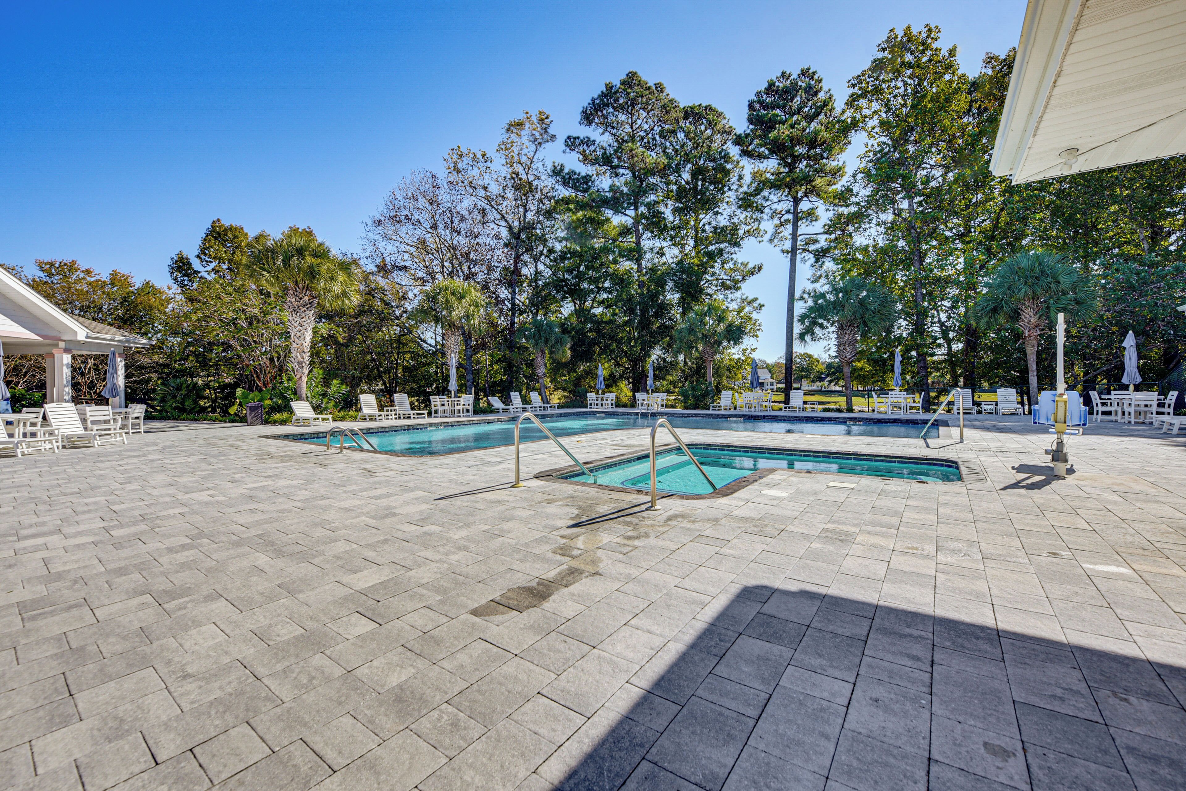 A swimming pool area with tiled flooring, lounge chairs, and umbrellas.