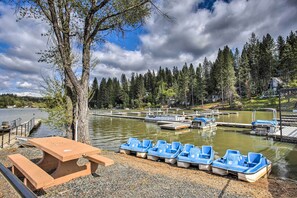 A lakeside area with a row of numbered blue boats, a picnic table, and a dock with a small building in the background. - Play Golf & Unwind! Pine Mountain Lake Family Home (Groveland)