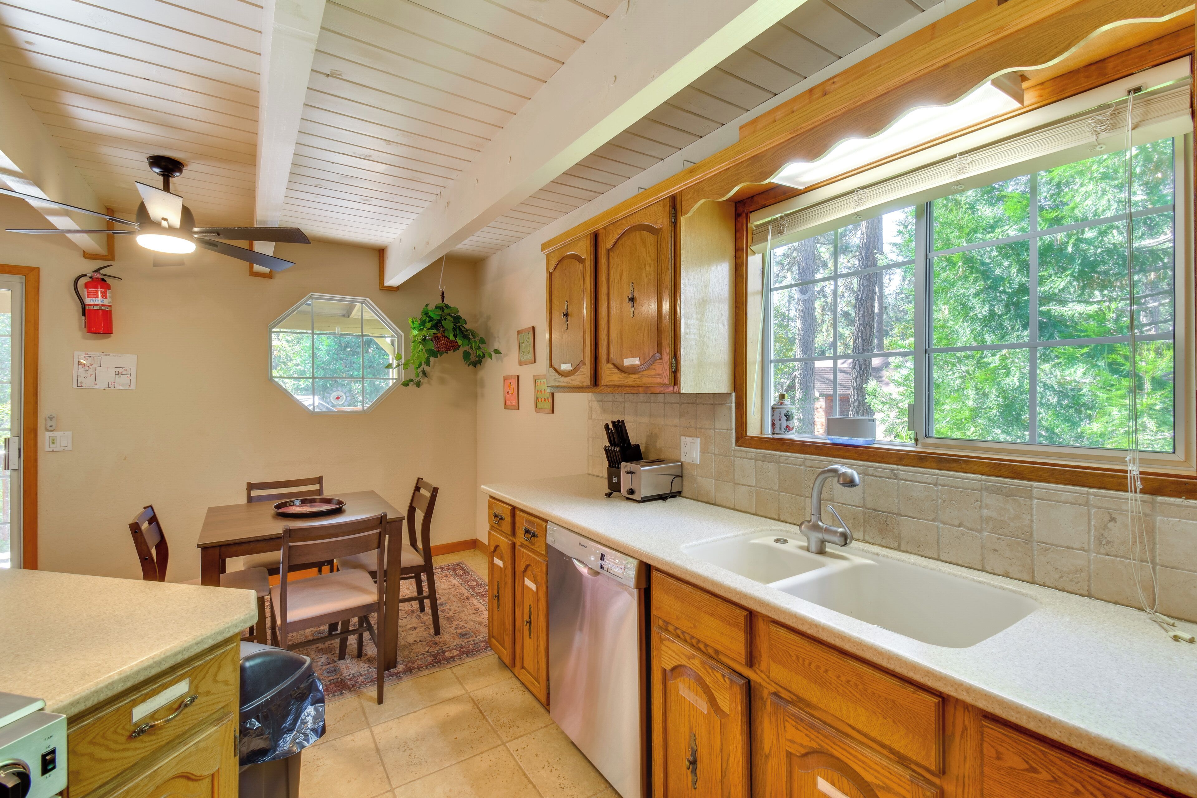 A kitchen with wooden cabinets, a dishwasher, a large window, and a ceiling fan.