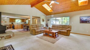 A spacious living room with a high ceiling, wooden ceiling beams, a fireplace, and a large window providing natural light. - Play Golf & Unwind! Pine Mountain Lake Family Home (Groveland)