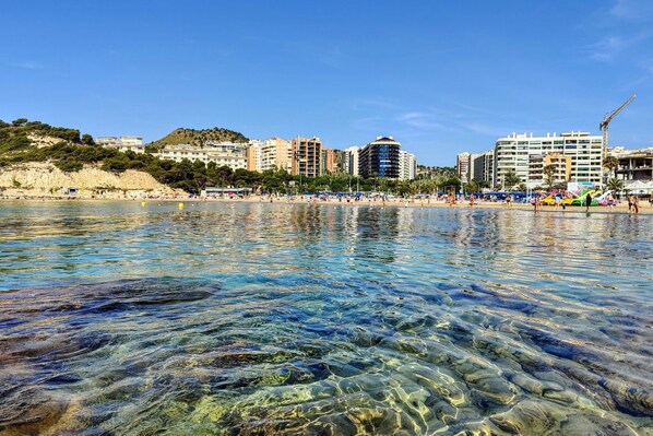 A coastal beach with clear water, buildings, and a hilly backdrop. - CALA ALTA vibe apartment (Alicante)