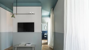 Ett modernt hotellrum med en säng, ett litet bord med böcker, en tv som är monterad på väggen och utsikt över badrummet.