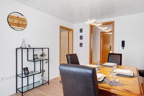 A dining area with a wooden table set for four, black leather chairs, a wall clock, and a black speaker.