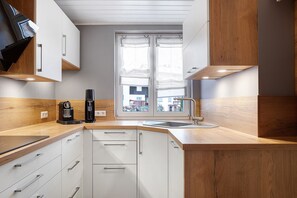 A modern kitchen with white cabinets, a wooden countertop, a coffee machine, and a window with curtains.