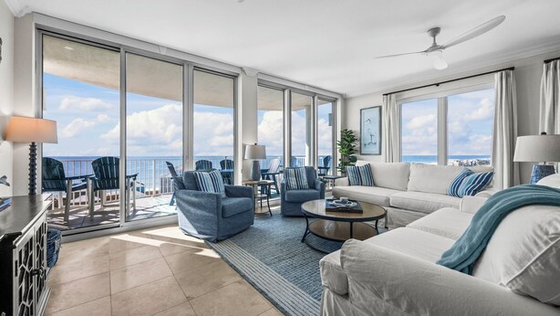 A spacious living room with a large sliding glass door leading to a balcony with a view of the ocean. There are several seating areas, including a sofa and chairs, and a coffee table. - High-end 4BR Condo w/ Gulf & Lagoon views, heated pool & hot tub (Gulf Shores)