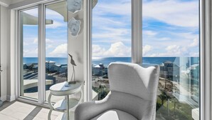 A modern room with a large window offering a view of the ocean and nearby buildings. - High-end 4BR Condo w/ Gulf & Lagoon views, heated pool & hot tub (Gulf Shores)