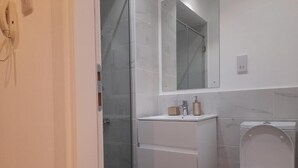 A bathroom with a shower, a sink with a mirror above it, and a toilet. - Cozy Nuggets at Embassy Gardens (Accra)