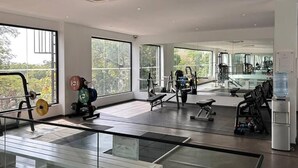 A modern gym with large windows, various exercise equipment, and a water dispenser. - Cozy Nuggets at Embassy Gardens (Accra)