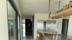A modern kitchen with a large island, stainless steel appliances, and a wooden shelf above the sink. - VILLA MAY, PRIVACY, FANTASTIC VIEWS AND 10 MIN FROM JAN THIEL (Willemstad)