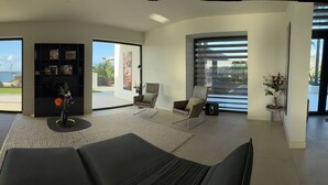 A spacious living room with a large window, a black bookshelf, and a view of the outdoors. - VILLA MAY, PRIVACY, FANTASTIC VIEWS AND 10 MIN FROM JAN THIEL (Willemstad)