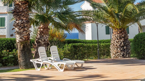 Un resort con palmeras, sillas de descanso blancas y vista al mar.