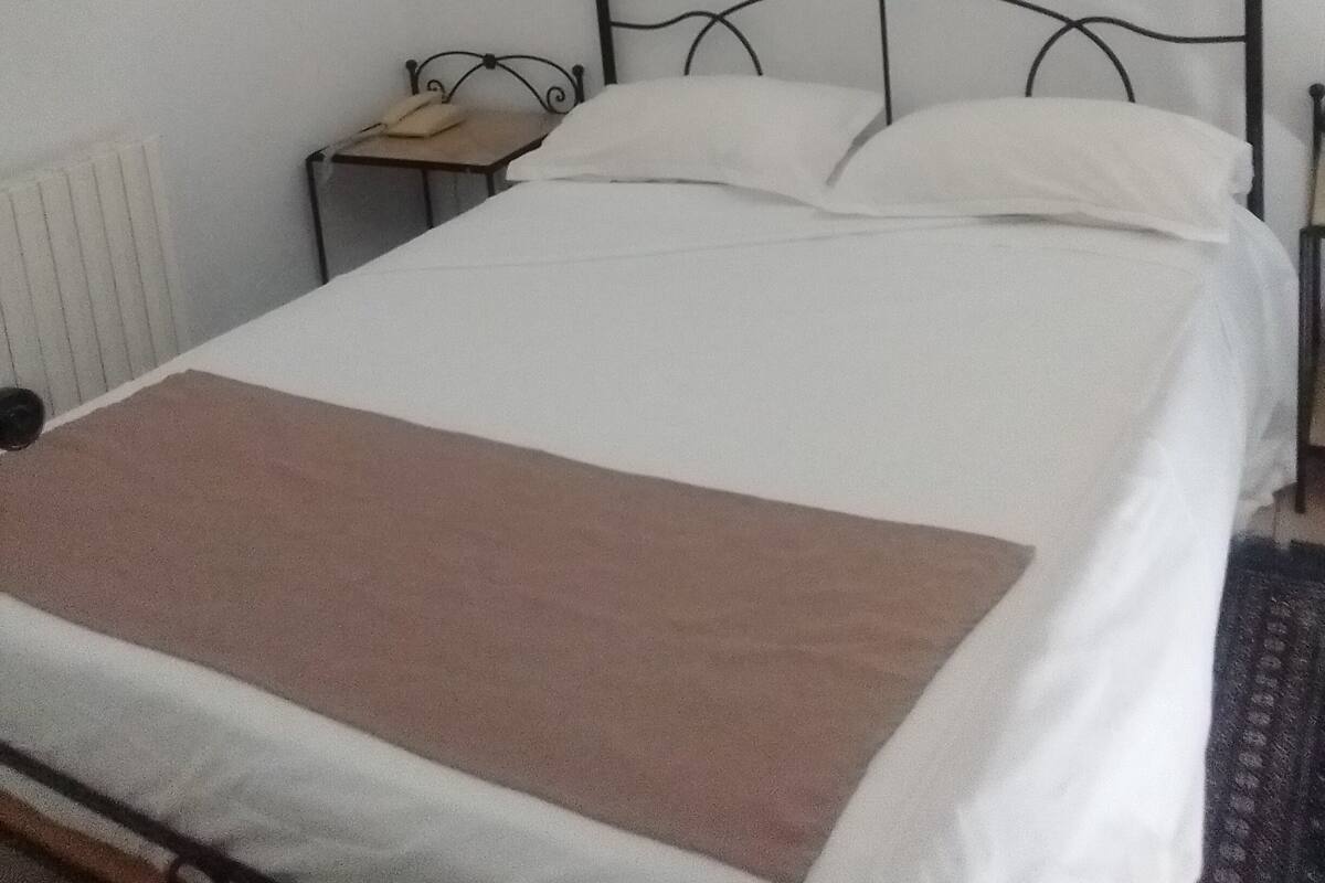 Un lit simple avec un cadre en métal, une table de chevet avec une lampe et un tableau encadré au mur.