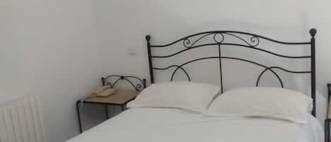 A single bed with a metal frame, a bedside table with a lamp, and a framed picture on the wall.