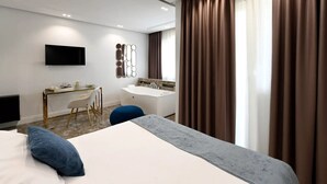 Una habitación de hotel moderna con una cama grande, un escritorio con una silla, una tocador con espejo y un televisor en la pared.
