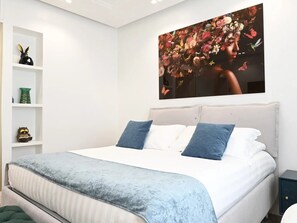 Un dormitorio con una cama grande, una mesita de noche, una estantería con adornos y un cuadro con motivos florales en la pared.