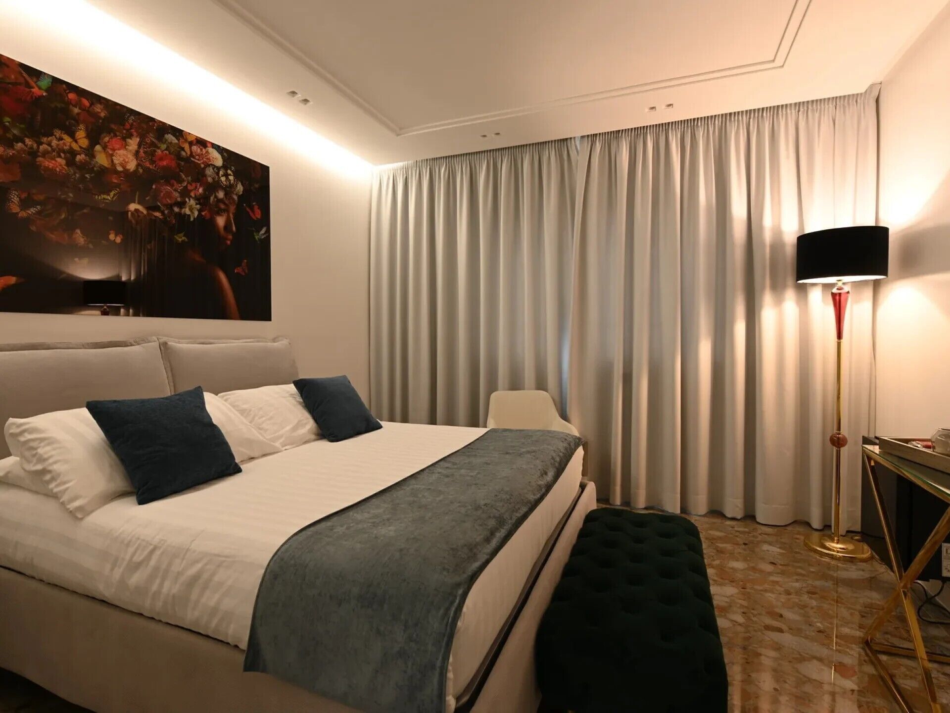 Een moderne hotelkamer met een groot bed, een bankje, een vloerlamp en een schilderij aan de muur.