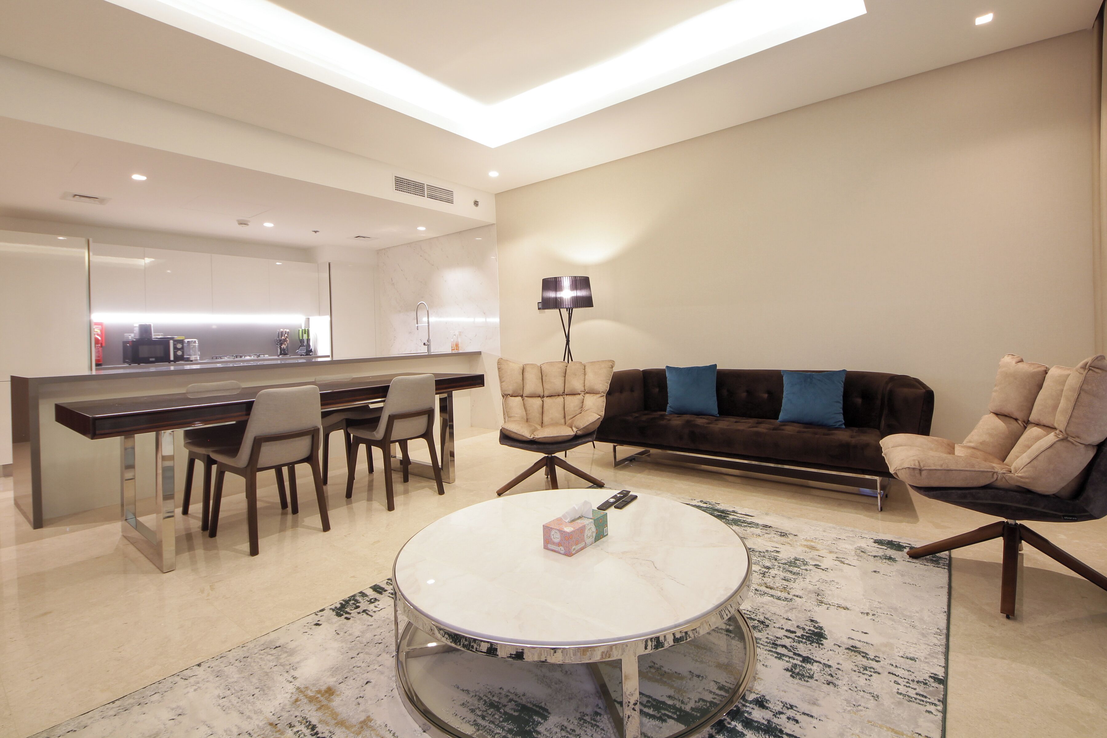 A modern living room with a round coffee table, a sofa, and a dining area with chairs and a kitchen in the background.